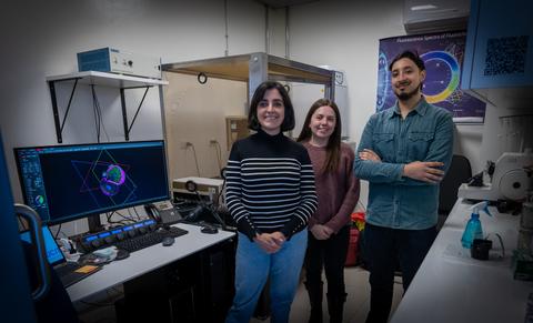 Un grupo de tres personas sonríe frente a una estación de trabajo en un laboratorio de investigación.