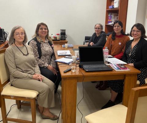 Un grupo de cinco mujeres se reúne alrededor de una mesa en un ambiente de trabajo.