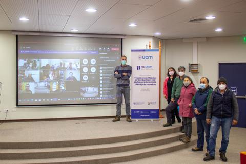 Un grupo de personas en una sala de conferencias con una presentación en pantalla y cada uno usando mascarillas.