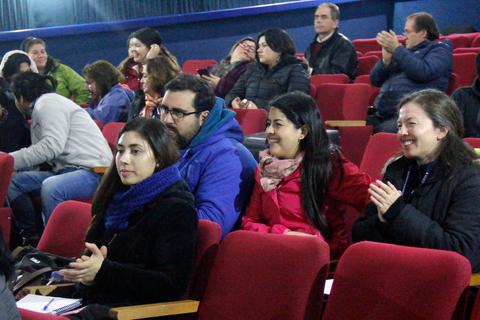 Un grupo de personas sentadas en un auditorio, algunas aplaudiendo y otras riendo.