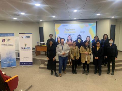 Grupo de personas posando en un evento académico con una presentación al fondo.