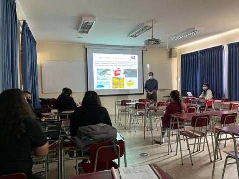 Un aula de clases con estudiantes sentados y un profesor frente a una pantalla de proyección.