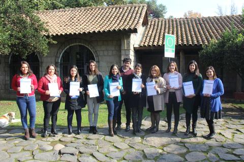 Un grupo de mujeres sostiene certificados frente a una casa con un jardín.
