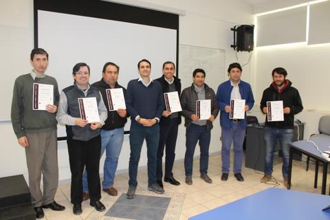 Un grupo de ocho hombres posando en una sala con certificados en la mano.