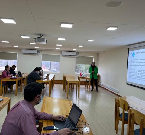 Una presentación en un aula con varios estudiantes y un expositor frente a una pantalla.