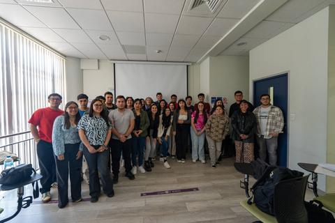 Un grupo de estudiantes posando juntos en un aula con una presentación de fondo.