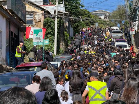 Una multitud se congrega en una calle estrecha, rodeada de edificios y vehículos.