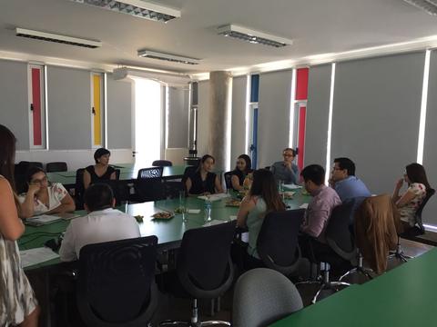 Un grupo de personas se reúne en una sala de reuniones, conversando mientras disfrutan de bocadillos.