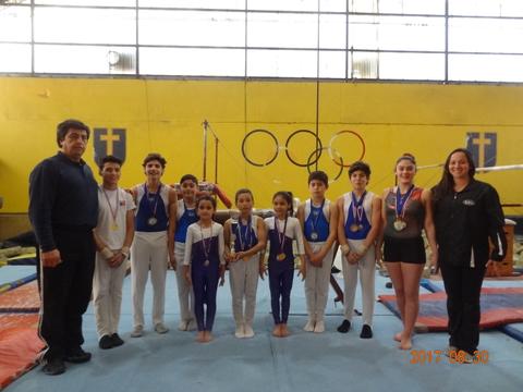 Un grupo de gimnastas jóvenes sonríen junto a sus medallas en un gimnasio.
