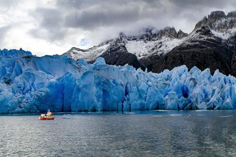 Un bote navega frente a un imponente glaciar azul en un paisaje patagónico.