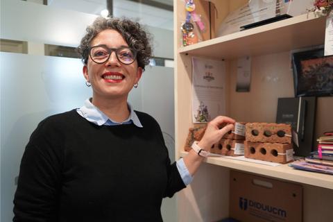 Mujer sonriente mostrando un objeto en un estante de oficina.