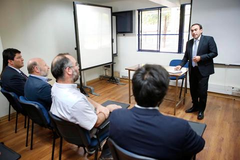 Un hombre está presentando frente a un grupo de cuatro personas en una sala de conferencias.