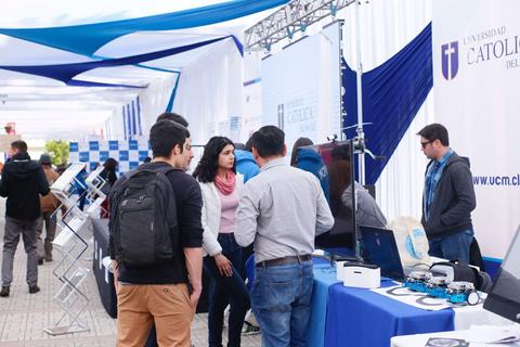 Un evento en la Universidad Católica donde varias personas interactúan con exposiciones tecnológicas.