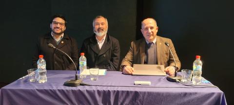 Tres hombres sentados detrás de una mesa en un evento.