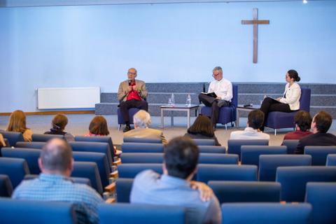 Un panel de discusión en un espacio religioso, con un público atento.