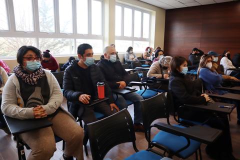 Un grupo de personas con mascarillas se encuentra sentado en un aula moderna.