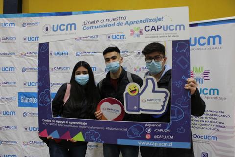 Un grupo de tres estudiantes se toma una foto en un evento de aprendizaje, sosteniendo un marco de fotografía de CAP UCM.