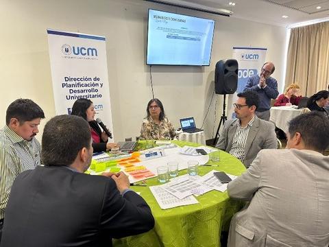 Reunión de trabajo con varios participantes discutiendo en una mesa sobre planificación universitaria.