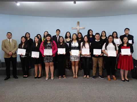 Un grupo de personas sonrientes sostiene diplomas en una ceremonia de graduación.