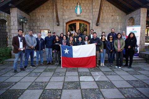 Un grupo de personas posa frente a un edificio mostrando una bandera de Chile.