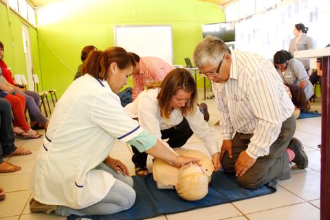 Un grupo de personas está aprendiendo RCP sobre un maniquí en una sala de capacitación.