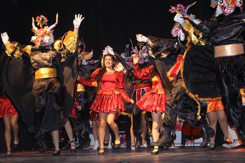 Un grupo de bailarines con trajes coloridos y máscaras participan en una presentación en un escenario.