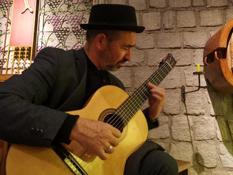Un hombre toca la guitarra en un ambiente acogedor con paredes de piedra.
