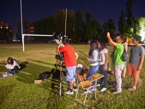 Un grupo de jóvenes observa el cielo nocturno usando un telescopio en un campo.