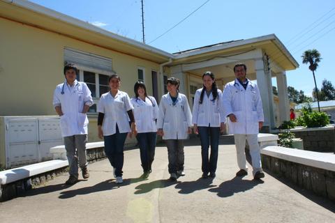 Seis profesionales de la salud caminan juntos frente a un edificio en un día soleado.