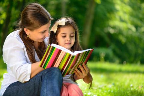 Una madre y su hija disfrutan leyendo un libro en un entorno natural.