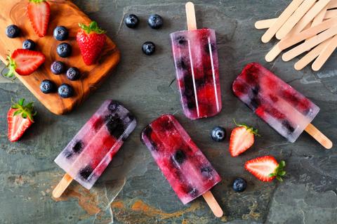 La imagen muestra helados de frutas con fresas y arándanos sobre una mesa de piedra.