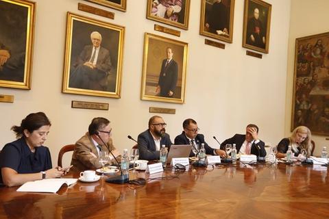 Una reunión formal en una sala con retratos históricos en las paredes.