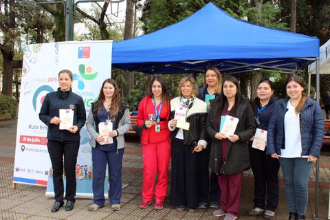 Un grupo de mujeres en un evento de salud bajo una carpa azul, sosteniendo folletos informativos.