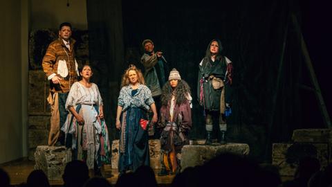 Un grupo de actores chilenos vestidos con trajes teatrales presenta una obra en el escenario.