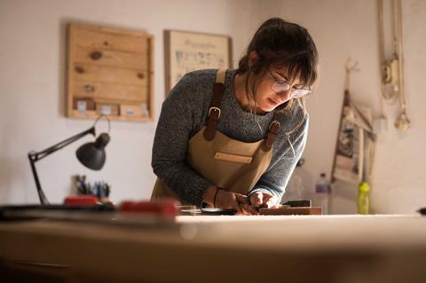 Una joven trabaja concentrada en un taller, utilizando herramientas sobre una mesa de madera.