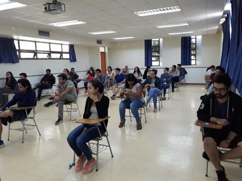 Un salón de clases con estudiantes sentados en pupitres durante una sesión.