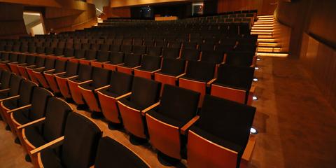 Una sala de teatro vacía con filas de asientos negros y una iluminación tenue.