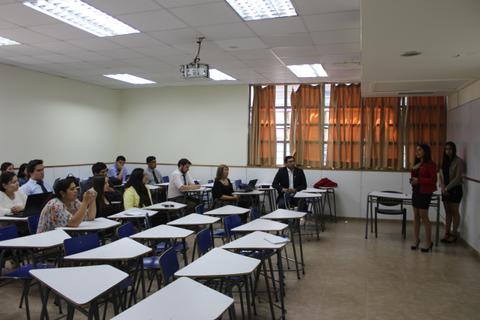 Un aula con estudiantes sentados y dos presentadoras frente a la clase.