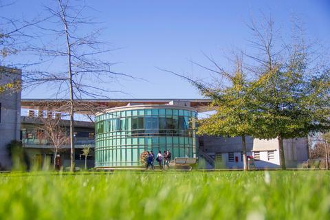 Una edificación moderna de vidrio rodeada de césped y árboles en un día soleado.