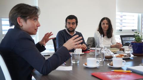 Una mujer habla apasionadamente mientras dos personas la escuchan en una reunión en una mesa.