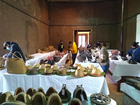 Un grupo de personas se encuentra trabajando en una sala rodeada de artesanías y sombreros en una mesa.