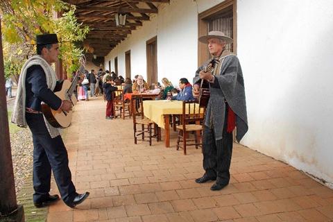 Dos músicos tradicionales tocan instrumentos en un entorno festivo y cultural.