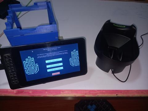 La imagen muestra un dispositivo móvil junto a un soporte y un cargador en una superficie de trabajo.