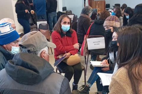 Un grupo de personas conversa en un salón, algunas usando mascarillas, mientras se enfocan en un tema específico.