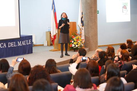 Una ponente está dando una charla en un auditorio mientras la audiencia la observa y graba la presentación con sus teléfonos.