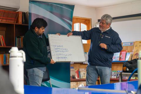 Dos hombres están presentando ideas en una pizarra durante una reunión en un espacio comunitario.