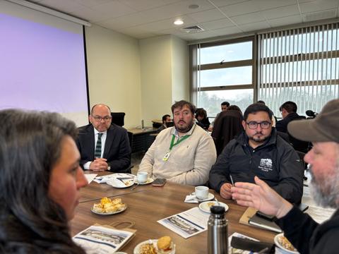 Un grupo de personas en una reunión con café y pasteles en la mesa.
