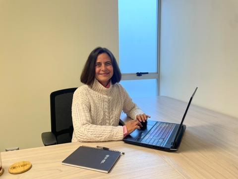 Una mujer sonriente trabaja en su laptop en una oficina con luz natural.