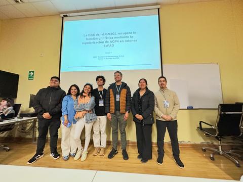 Un grupo de jóvenes se encuentra posando frente a una presentación en un evento académico.