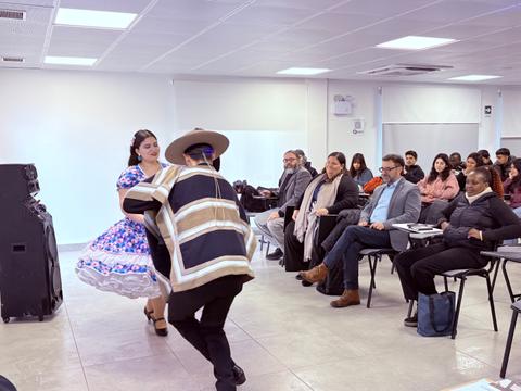 Una pareja baila una danza folclórica chilena mientras un público atento observa.